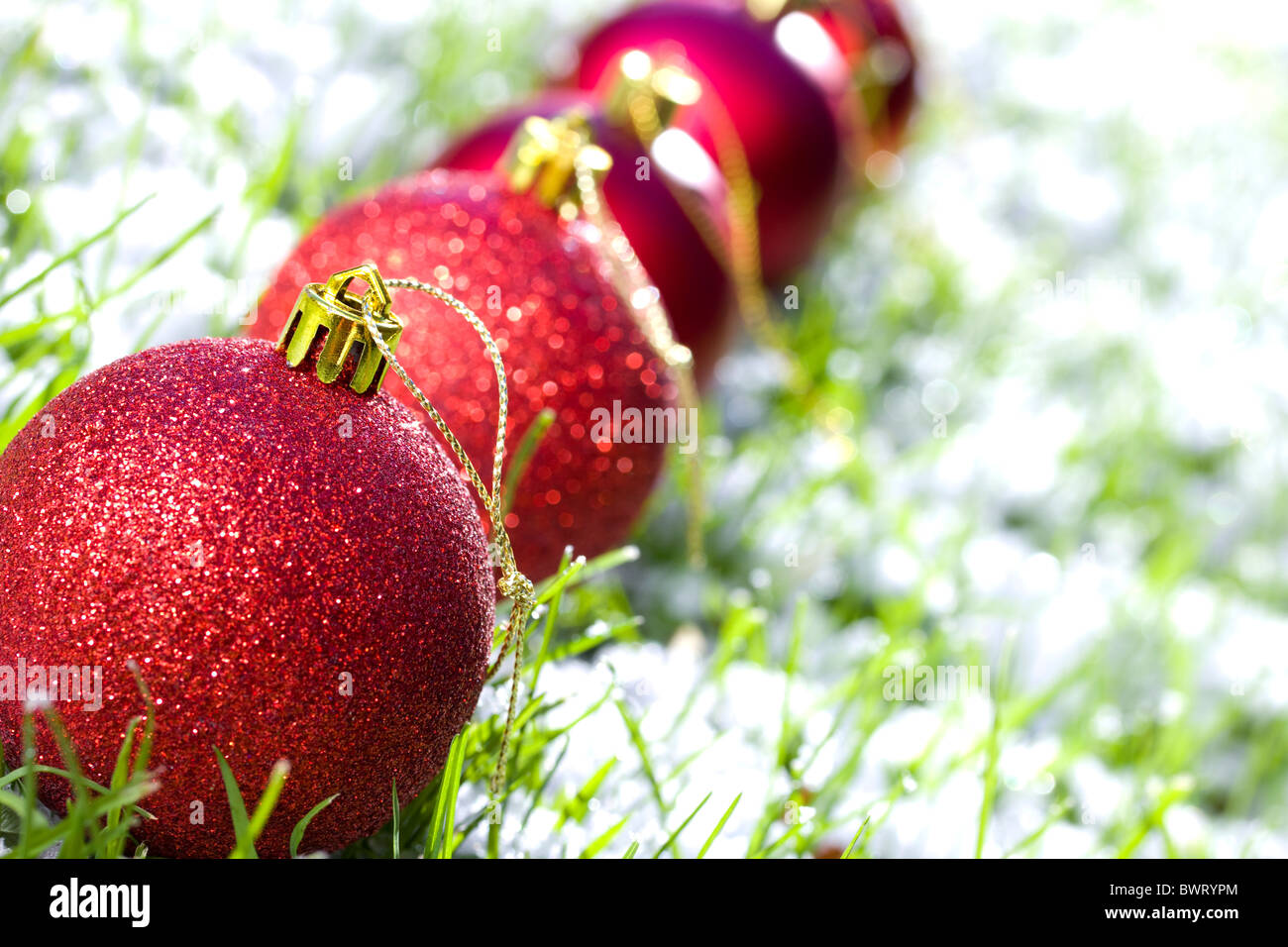 row of Christmas balls with snow and frozen grass focus on first ball Stock Photo