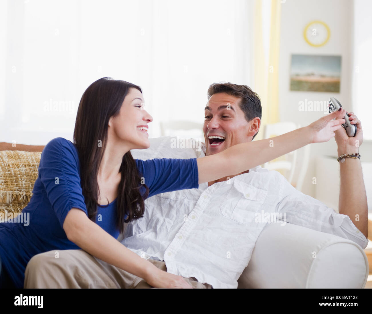 Laughing mixed race man keeping remote control away from wife Stock Photo