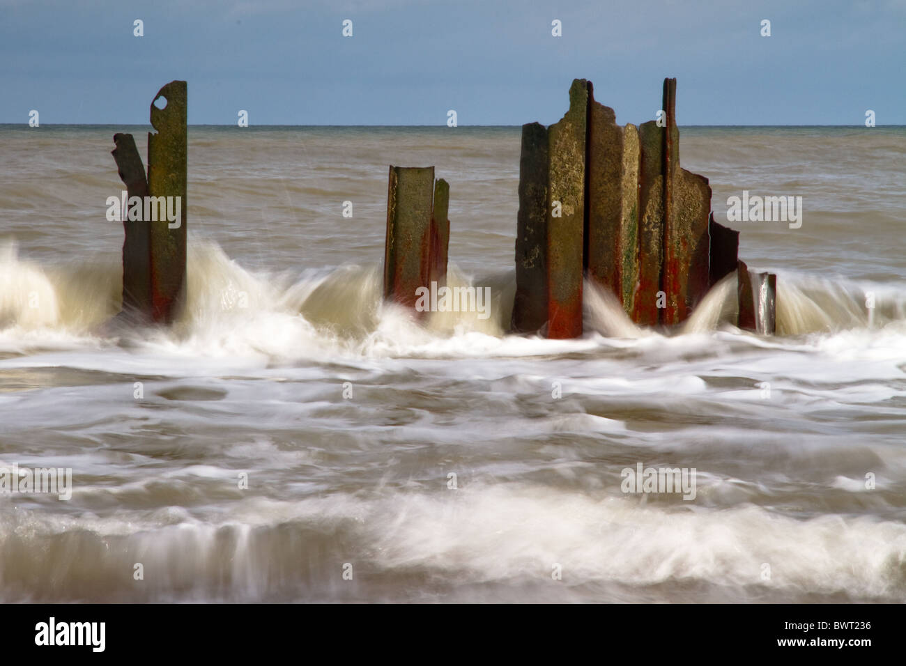 A wave streams through abandoned iron sea defenses on Happisburgh beach ...