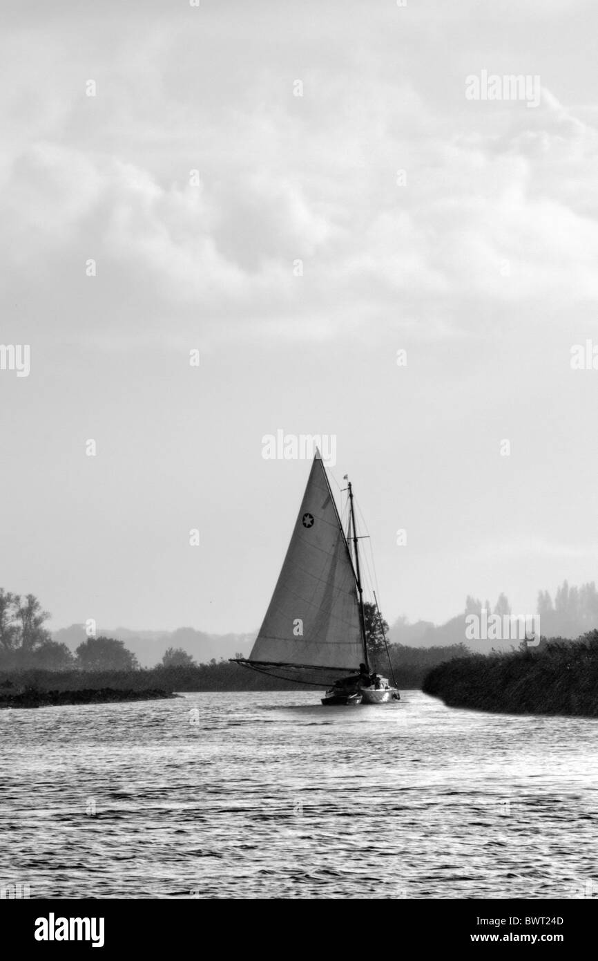 A classic sailing boat reaches down a river in the Norfolk Broads Stock Photo