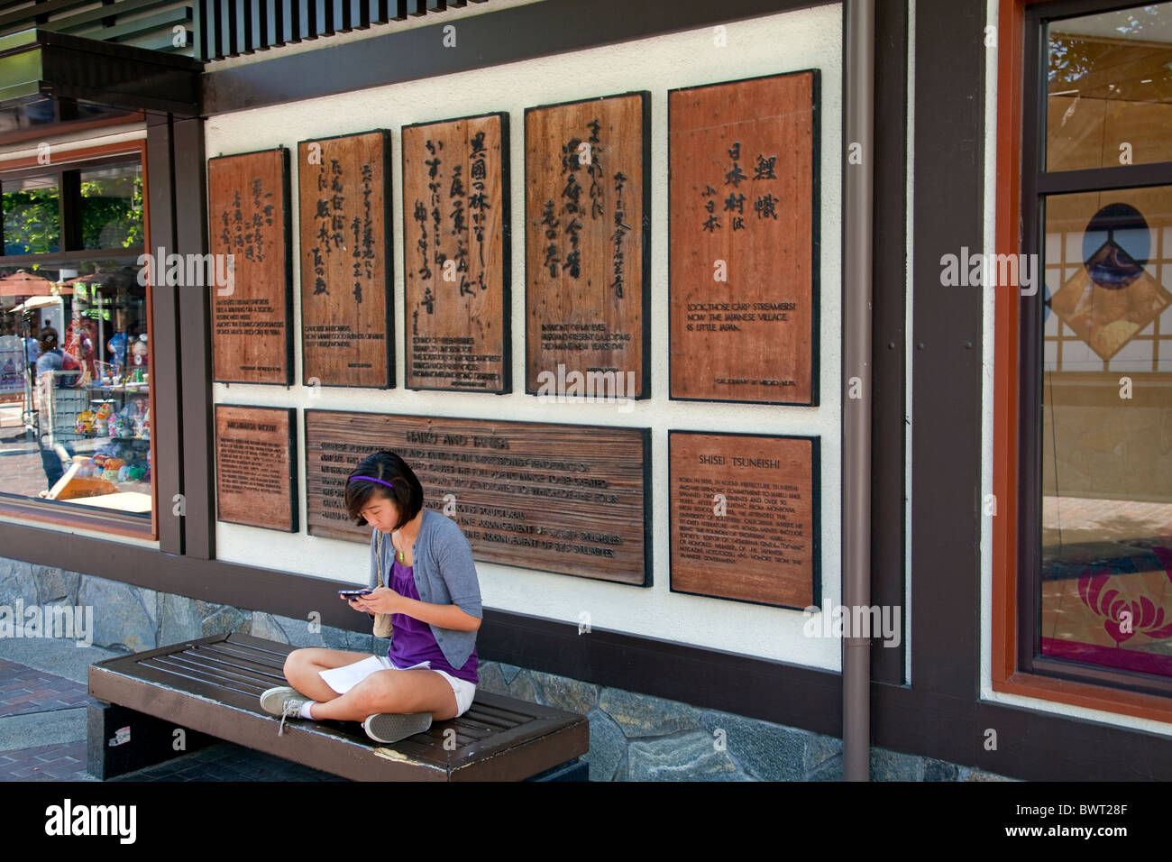 Girl sitting in front of wooden tablets of Haiku poems. Japanese Village Plaza, Little Tokyo, Los Angeles, California, USA Stock Photo