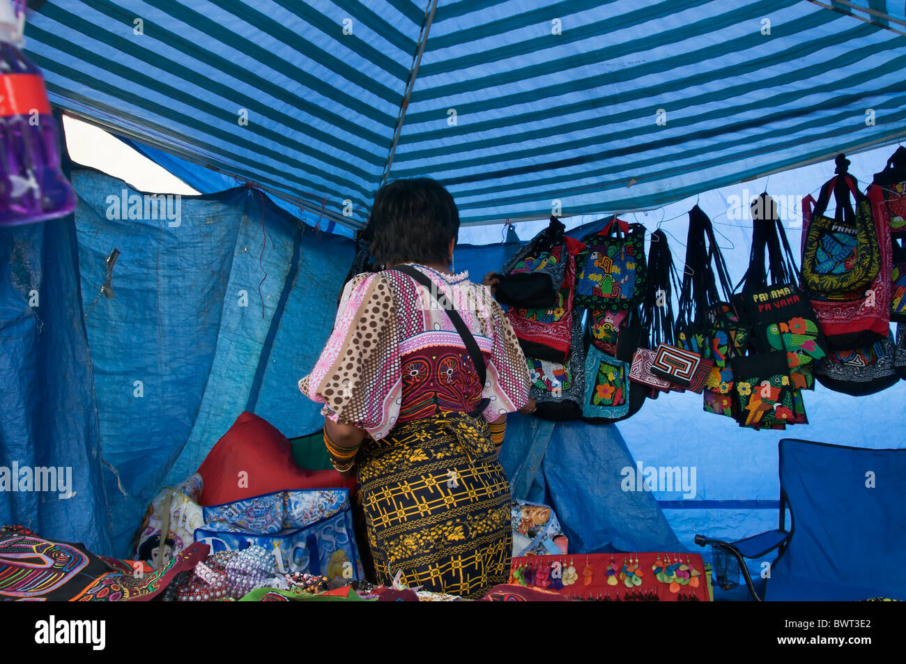 A Kuna woman in traditional costume sells handicrafts made from molas at a covered stall in Pedasi, Panama. Stock Photo