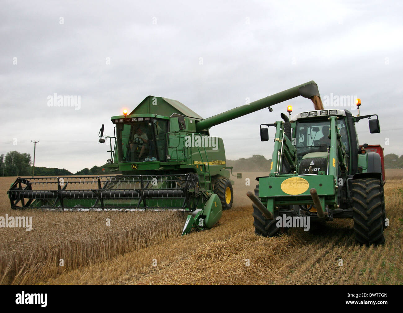 John Deer green combine harvester and a green tractor in a field cutting the harvest Stock Photo