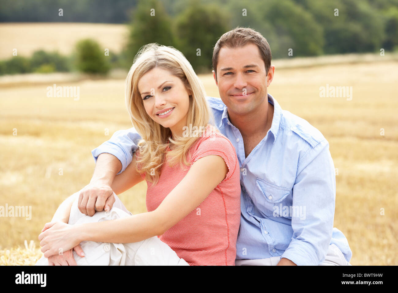 Couple Sitting On Straw Bales In Harvested Field Stock Photo