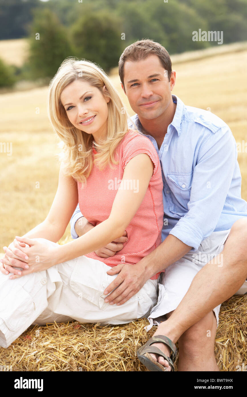 Couple Sitting On Straw Bales In Harvested Field Stock Photo