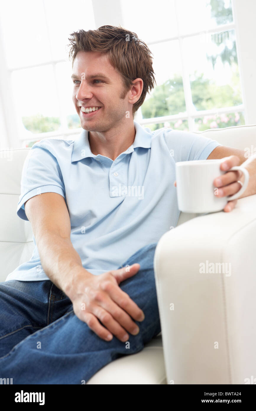 Man Sitting On Sofa Drinking Coffee Relaxing At Home Stock Photo