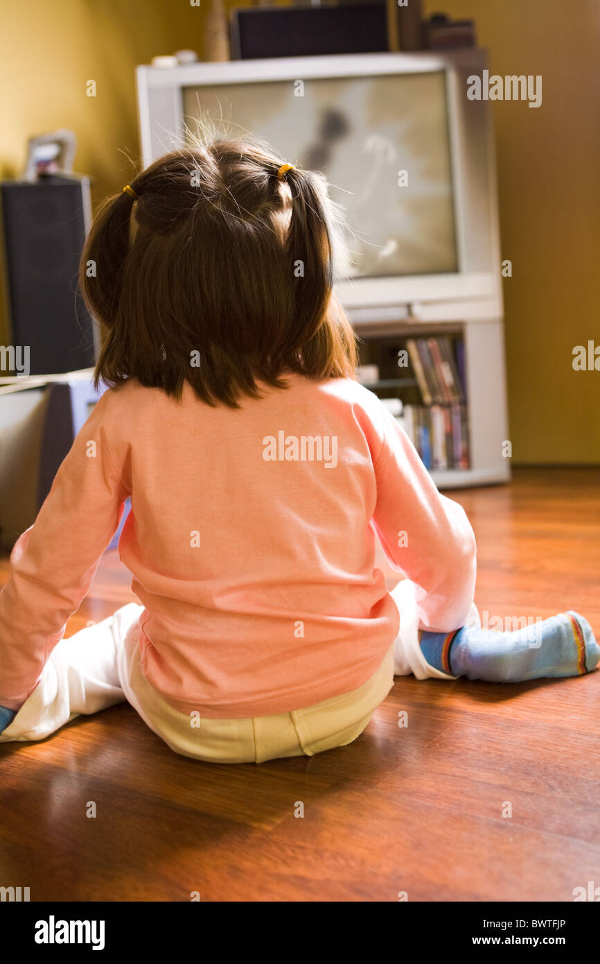 Rear view of little girl sitting on the floor and watching cartoons on ...