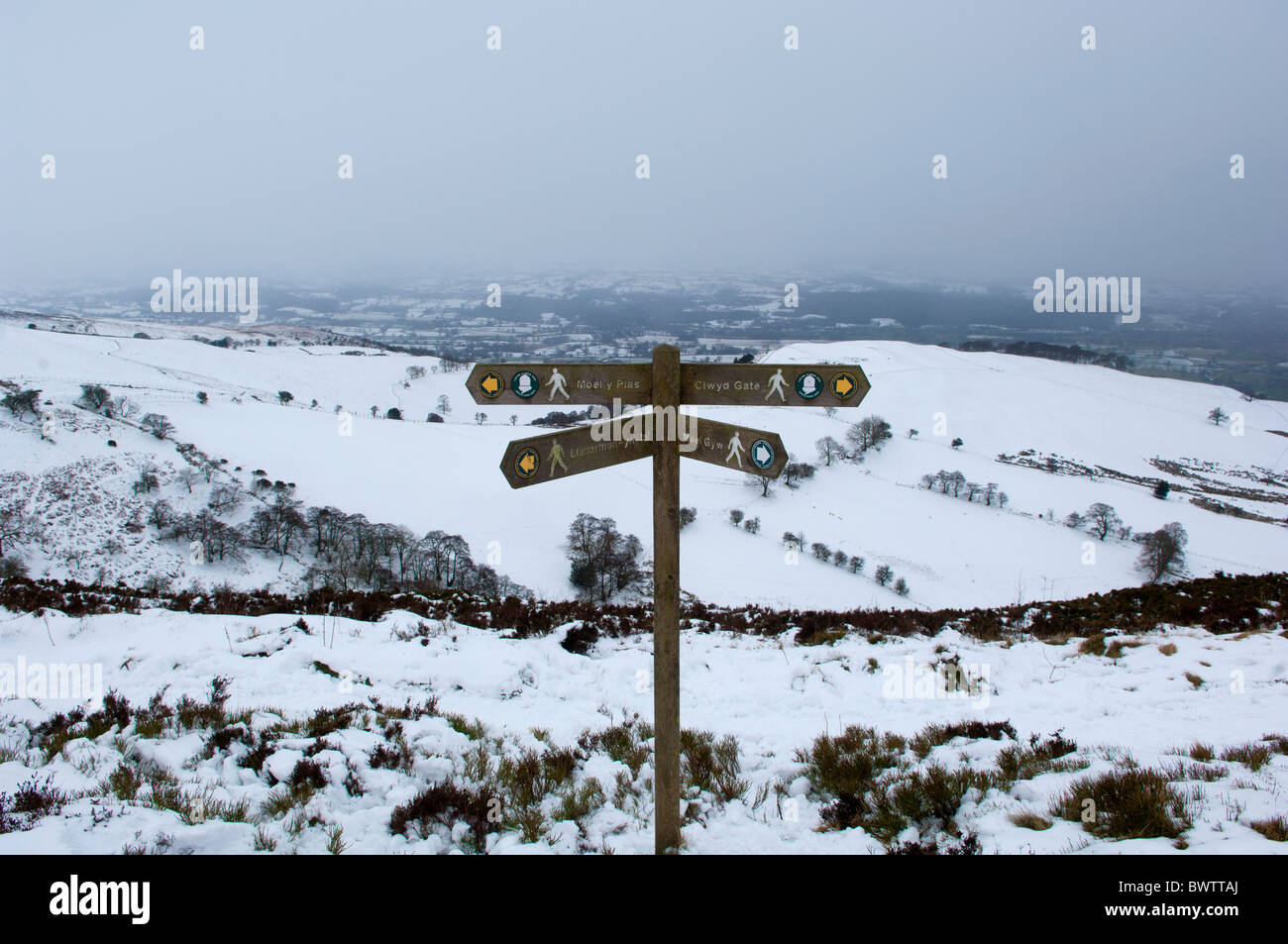 A snowy winter scene showing a finger post on Offas Dyke footpath nr Moel Gwm. Vale of Clwyd visible in distance Stock Photo