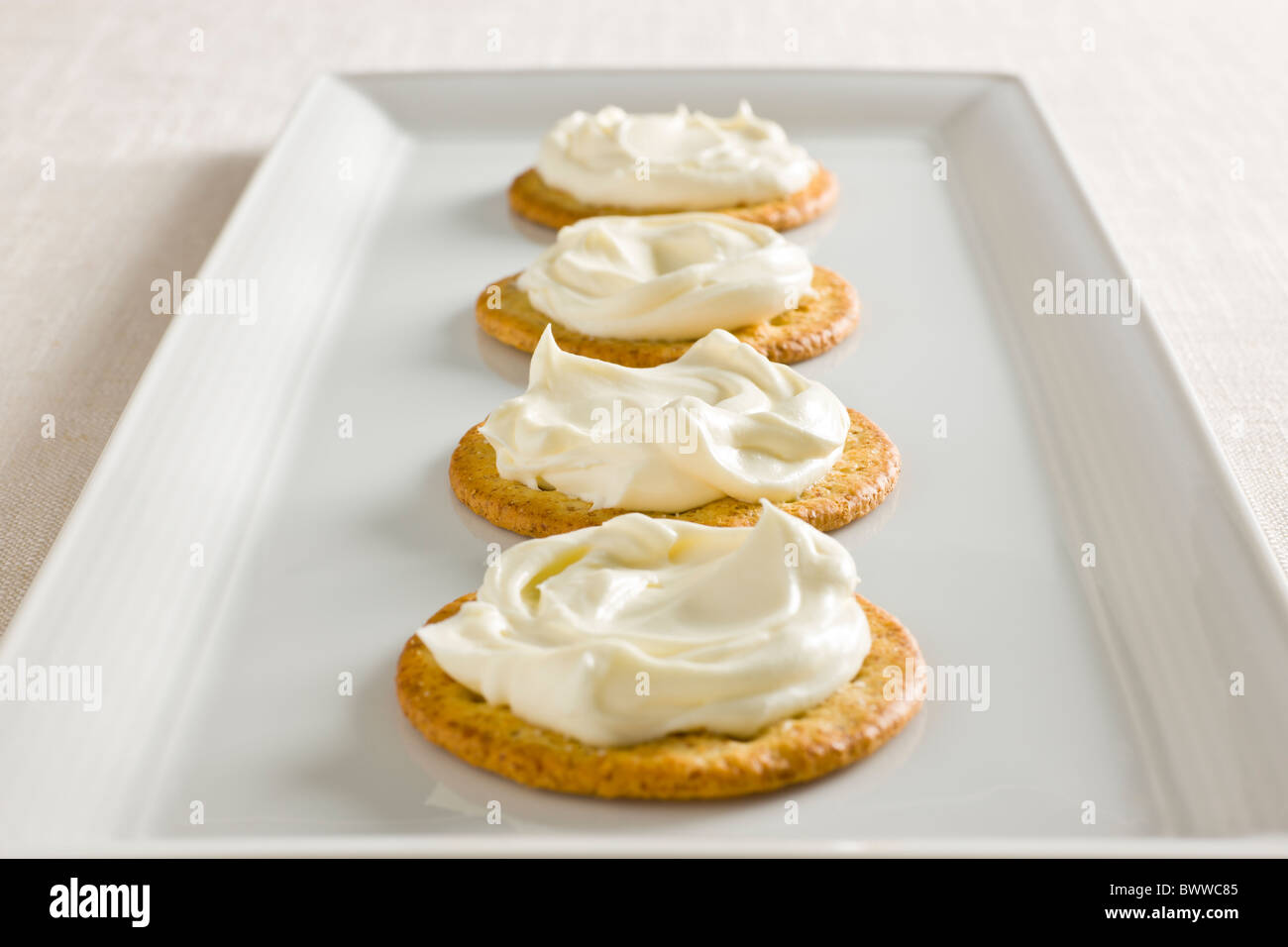 Crackers with Creamy Cheese spread on top on a white rectangular