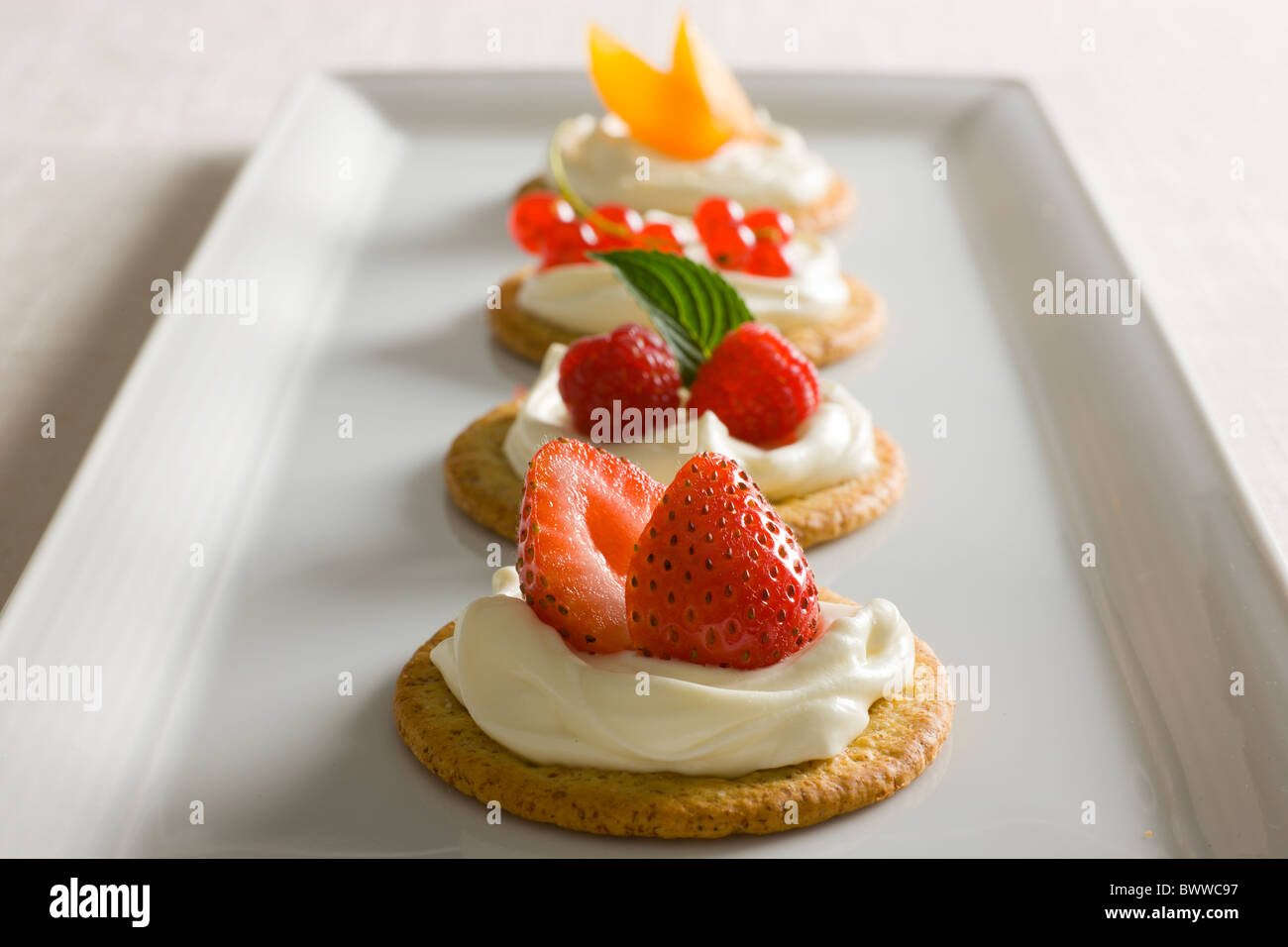 Crackers with Creamy Cheese spread, garnished with Raspberries, Mint, Strawberries, Red Currant and Yellow Plums on top on a whi Stock Photo