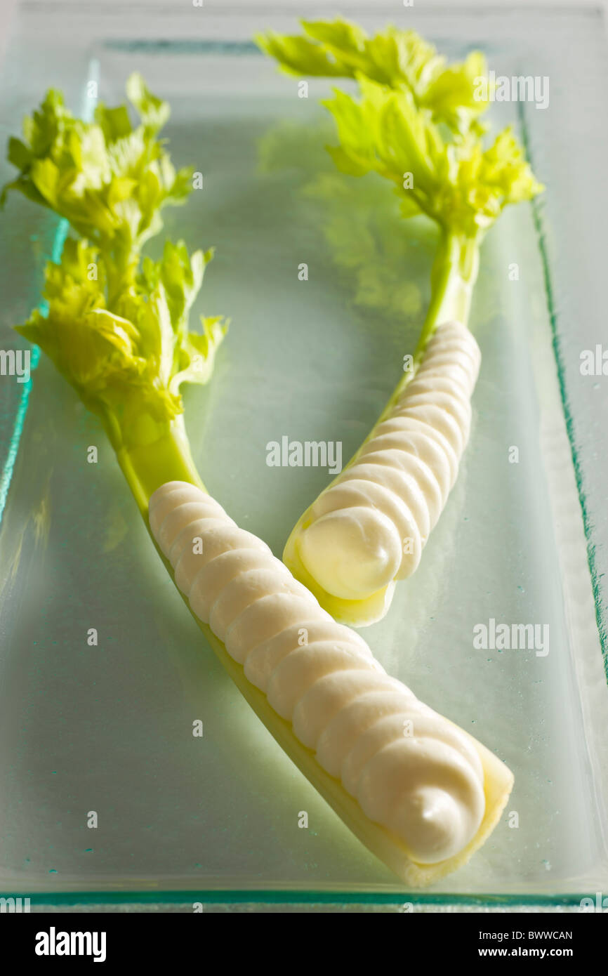 Two stalks of celery heart with cream cheese piped in it's cavity on a glass plate, over a white background. Stock Photo