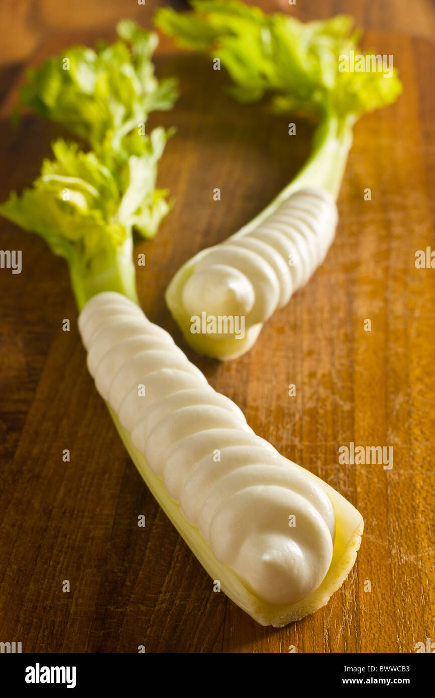 Two stalks of celery heart with cream cheese piped in it's cavity over a wood board. Stock Photo