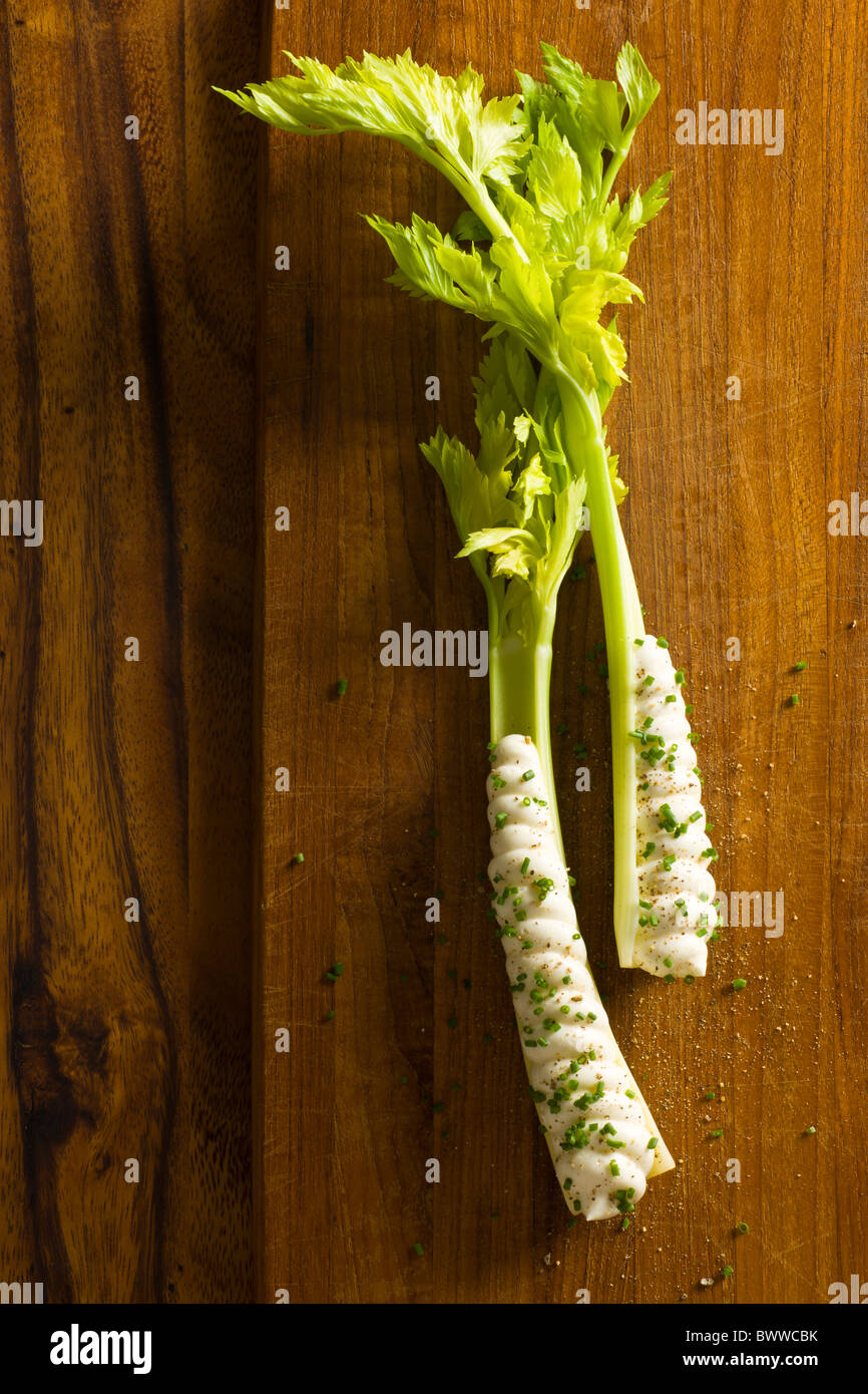 Two stalks of celery heart with cream cheese piped in it's cavity over a wood board. Stock Photo