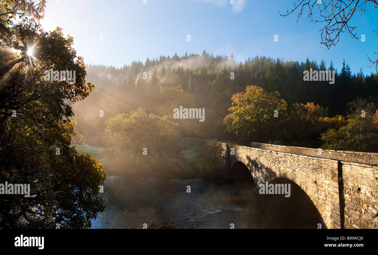 Bridge over The Afon Llugwy on the A5 between Betws y Coed and Capel Curig, North Wales. Sun through trees and rising mist Stock Photo