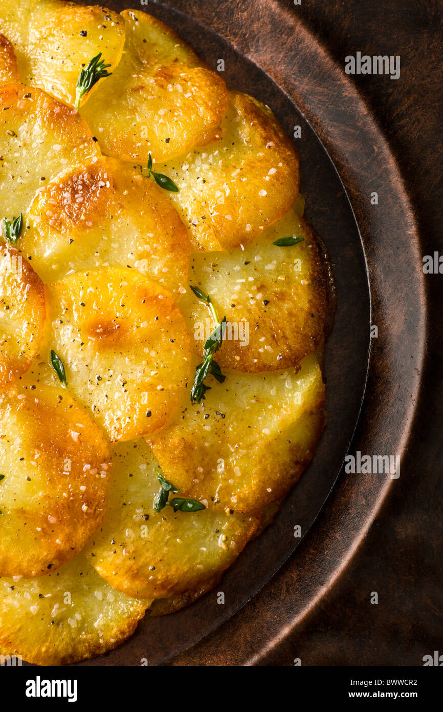 Potato Galettes or Anna garnished with fresh thyme, salt and pepper and served on a rustic plate. Stock Photo