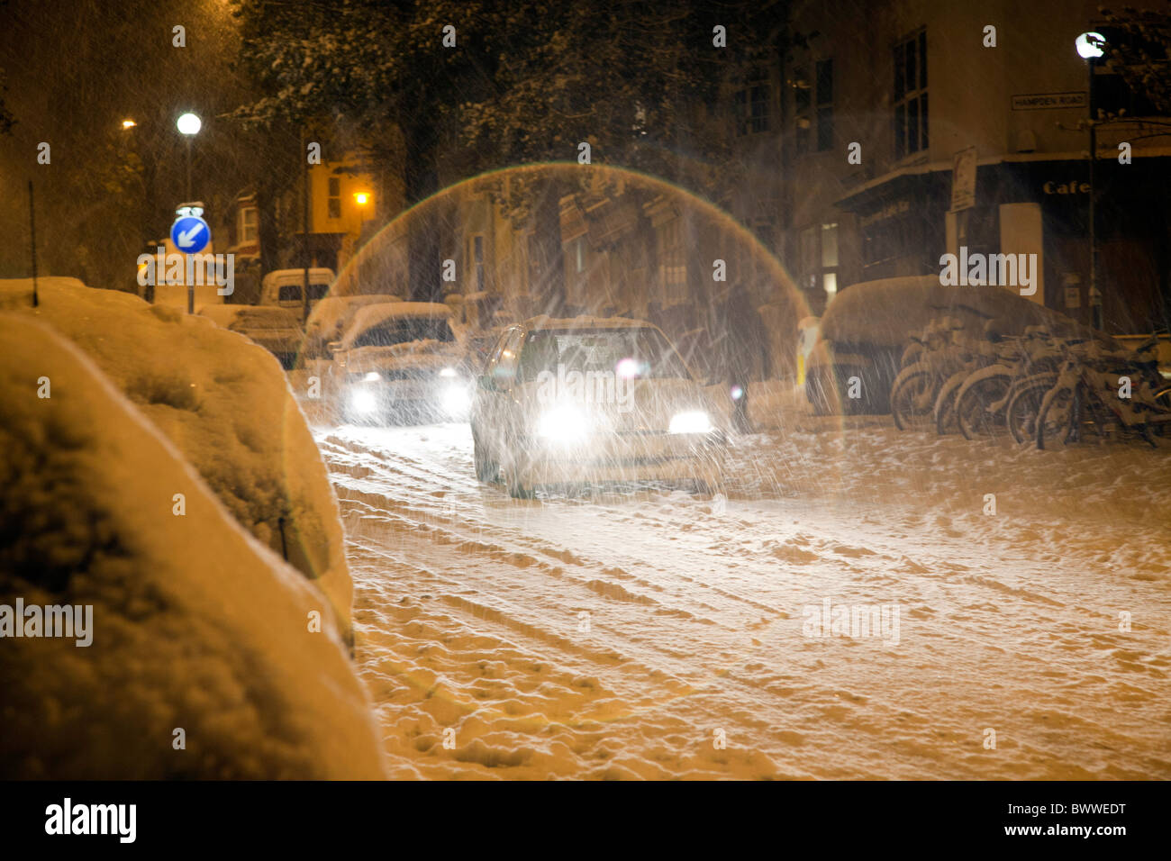 Cars drive slowly down a hill covered with freshly laid snow in a