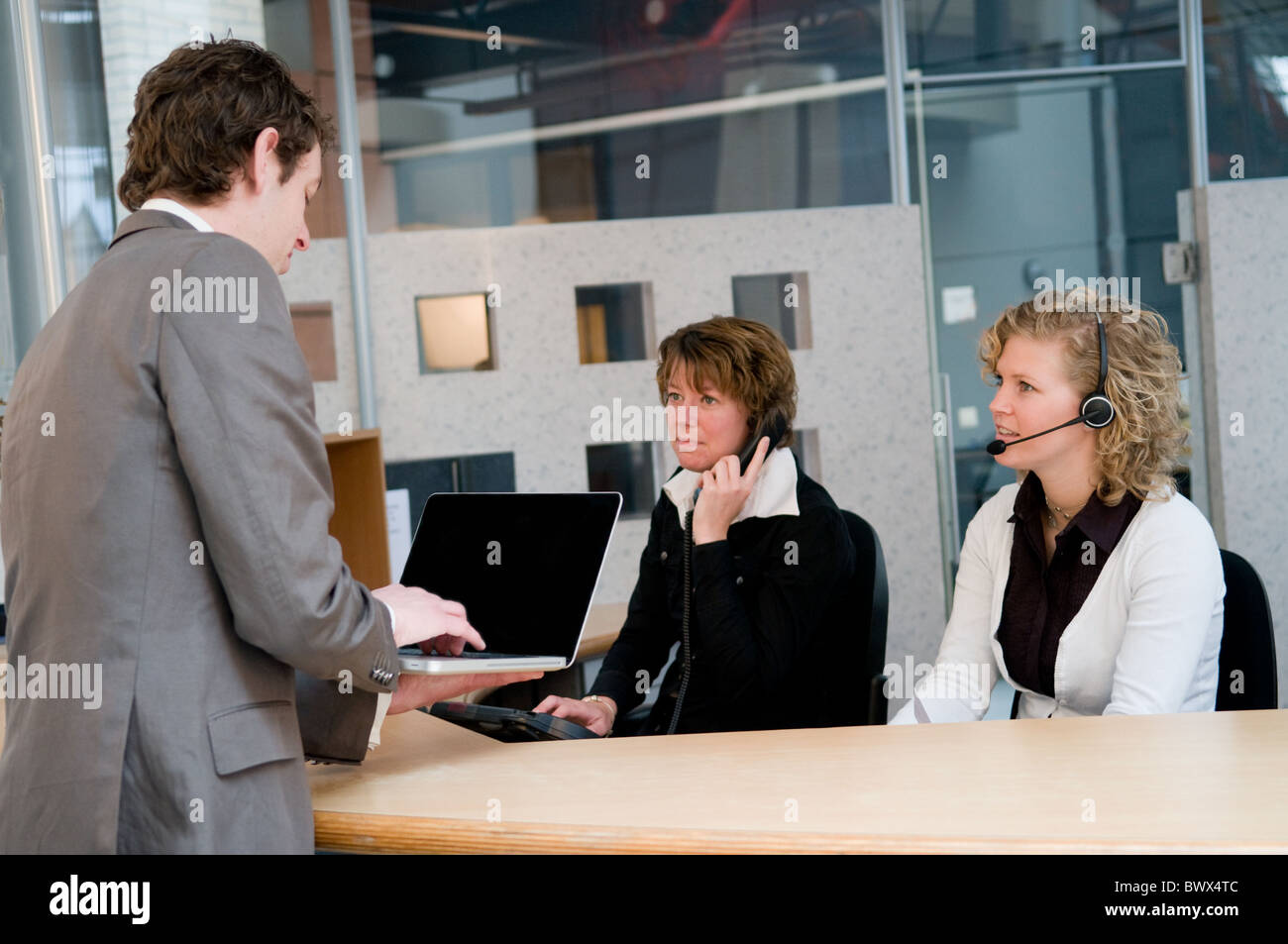 Client coming at the receptionist working at a helpdesk Stock Photo - Alamy