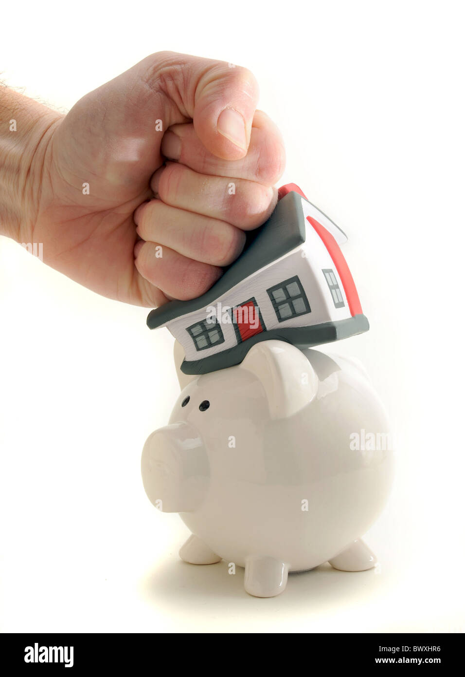HOUSE HIT AND SQUASHED BY MANS HAND ON PIGGY BANK RE SAVINGS HOUSING MARKET MORTGAGES HOUSE PRICES ETC UK Stock Photo