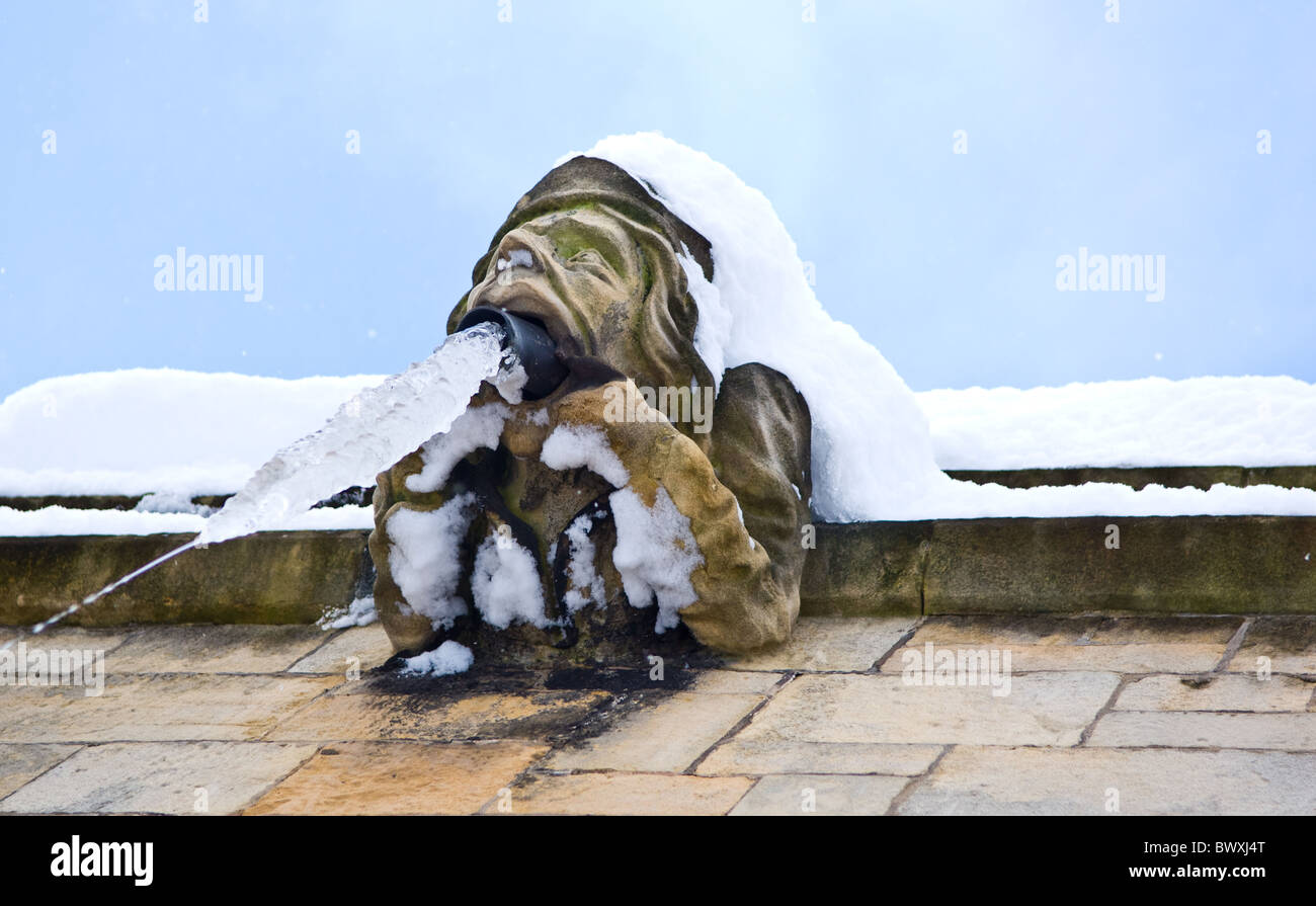 Frozen roof drainage pipe coming out of the mouth of a church gargoyle Stock Photo