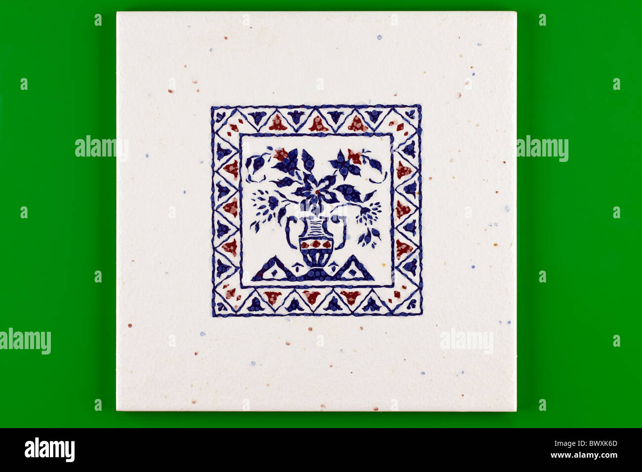 Blue and white pattered square ceramic tile on a green background Stock Photo