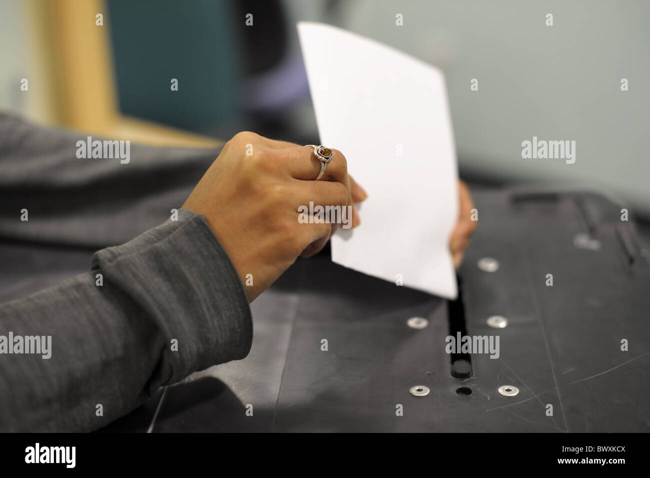 Young Asian woman's hand holding a ballot paper as she casts her vote and puts it into a black ballot box at an election Stock Photo