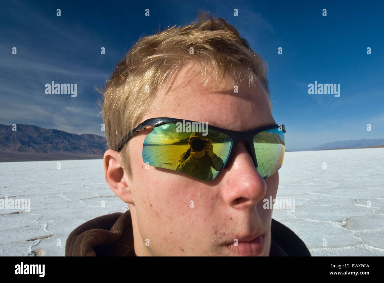 Photographer's image reflected in glasses of teenager hiker at Salt Flats,  Badwater area, winter, Death Valley, California, USA Stock Photo