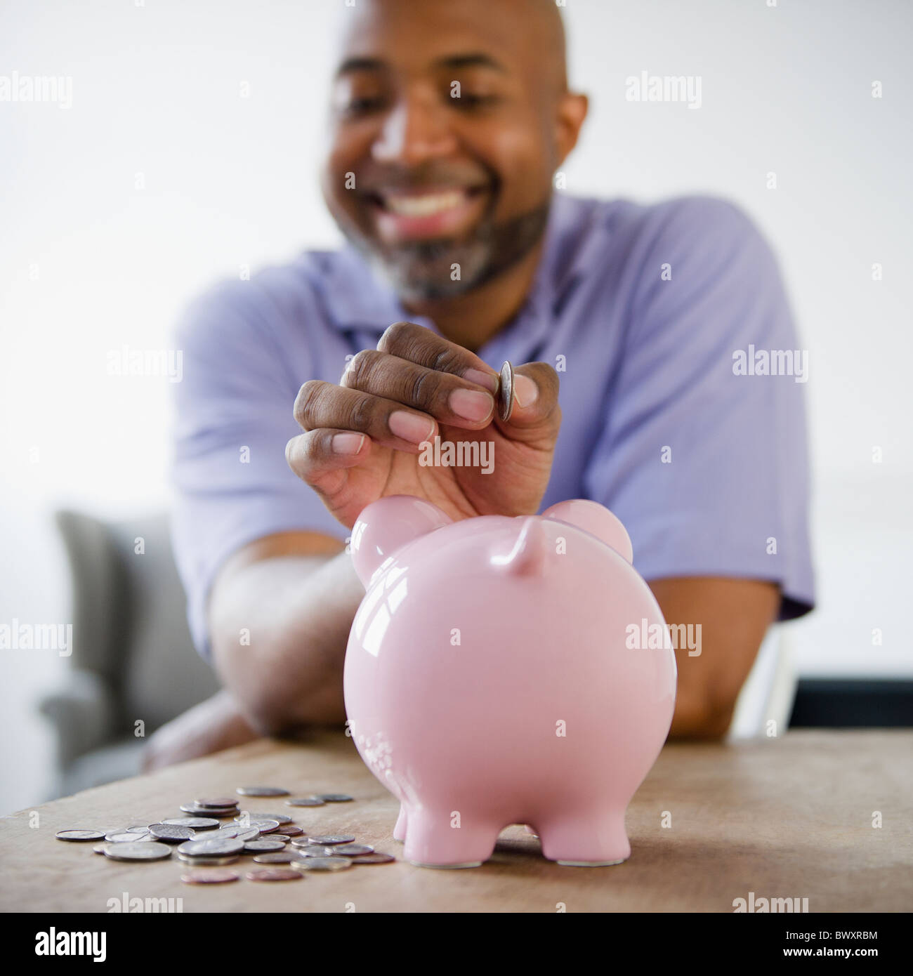Smiling African American man putting coins in piggy bank Stock Photo ...
