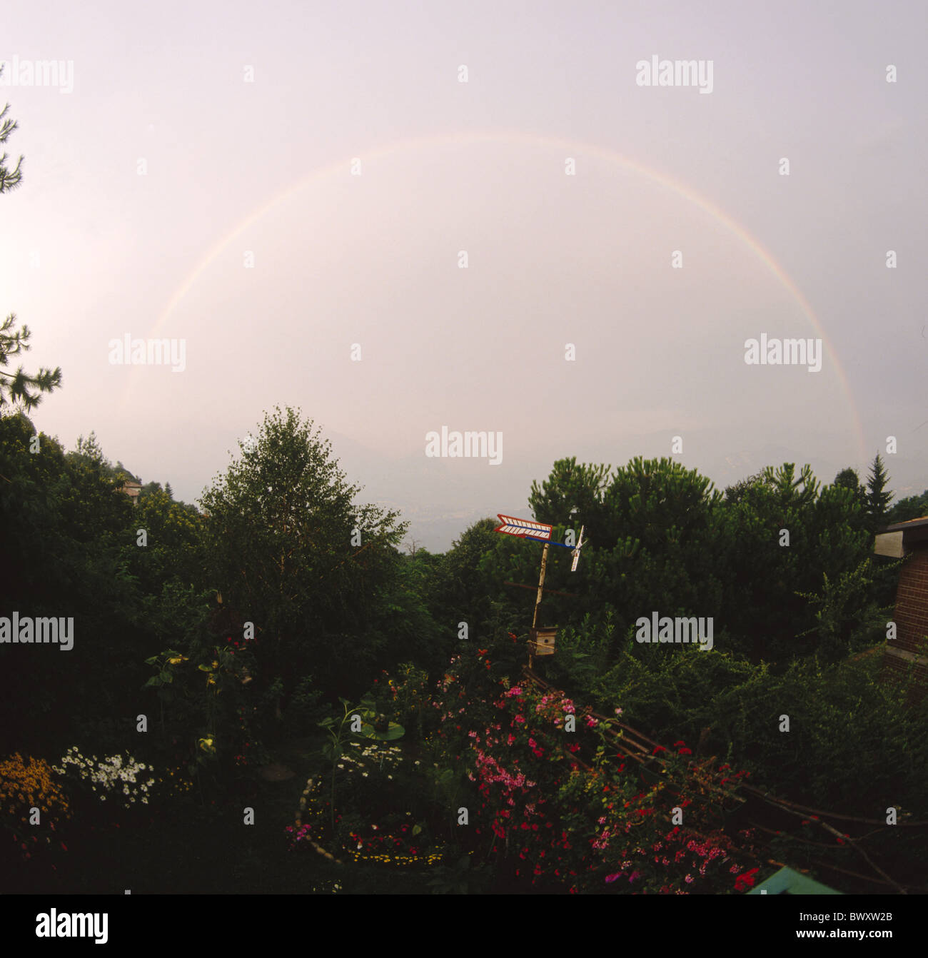 evening pale thunderstorm rainbow round arch allotment garden Switzerland Europe Ticino weathervane Stock Photo