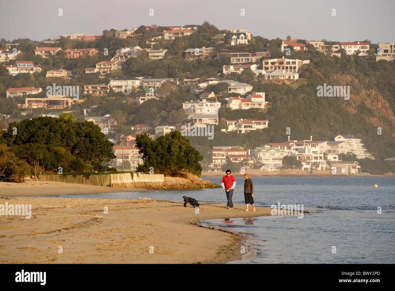 Couple walking their dog along the beach of Leisure Isle in Knysna on the Garden Route in South Africa. Stock Photo