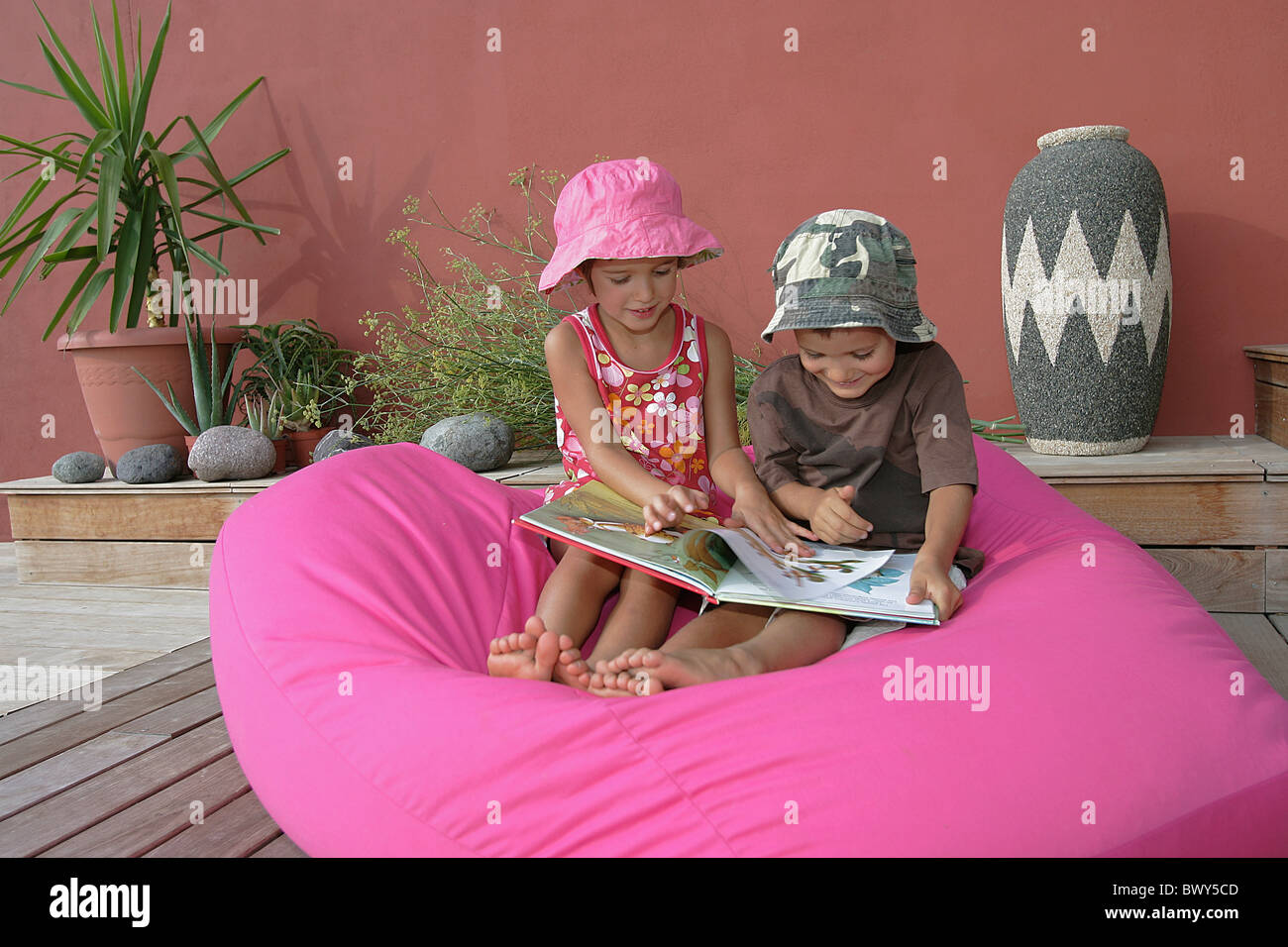 Two young child,brother and sister reading a book together on a pink pouf Stock Photo