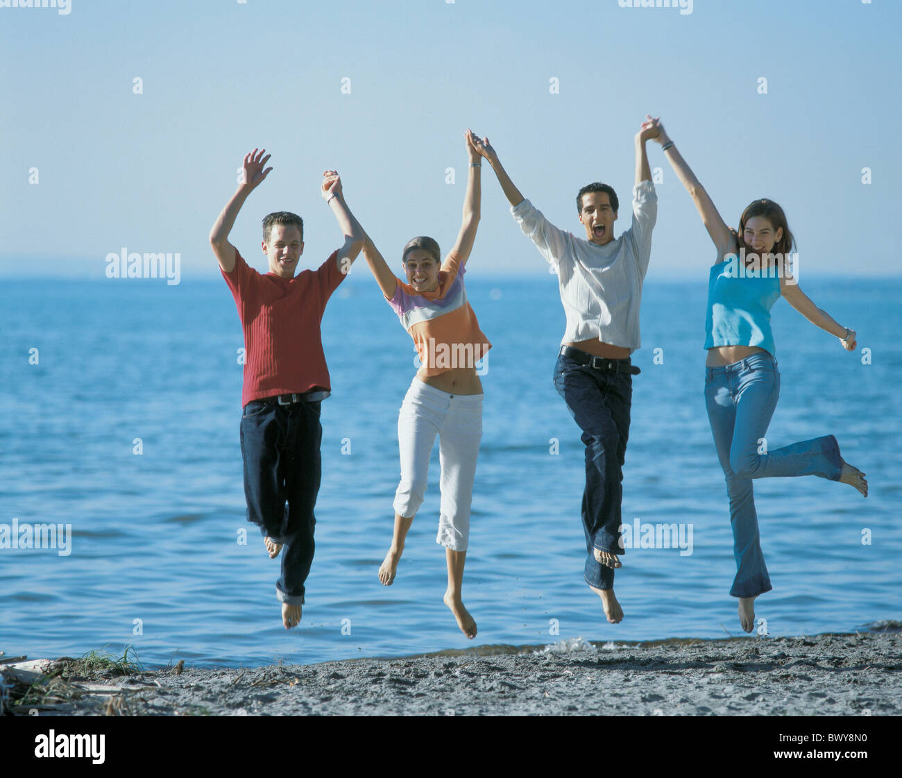 beach couples group high jumping hochspringen jump lake Laughing outside seashore shore teenagers Two p Stock Photo