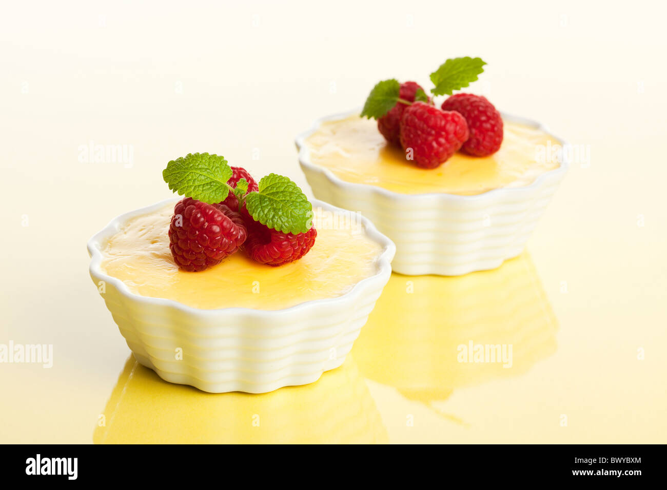 two bowls of vanilla custard garnished with raspberries on reflective bright yellow surface, selective focus Stock Photo