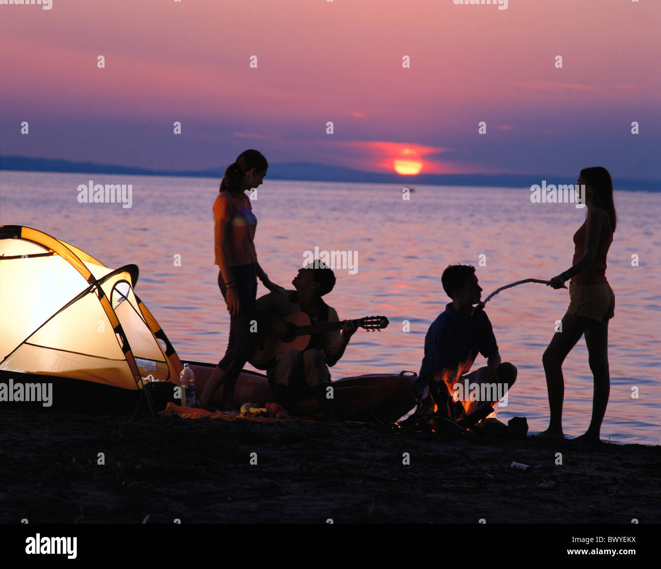 youngsters tents camping campinging camp warehouse food guitar campfire lake sea lake shore sundown tee Stock Photo