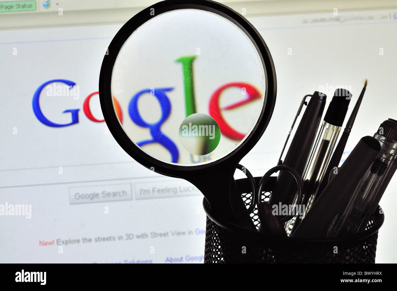 Desk top tidy ,silhouette Pens, Biro, Scissors , Magnifying glass ,backdrop computer screen displaying distorted Google logo Stock Photo