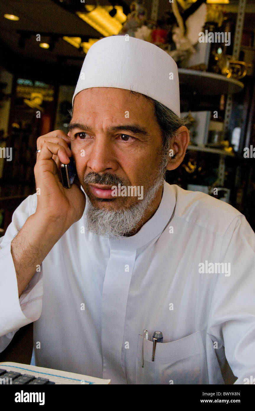 Distinguished older Muslim man in shop in Arab quarter Singapore talking on cell phone Stock Photo
