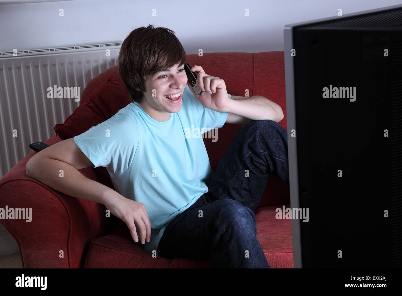Young male holding a phone smiling and watching tv Stock Photo
