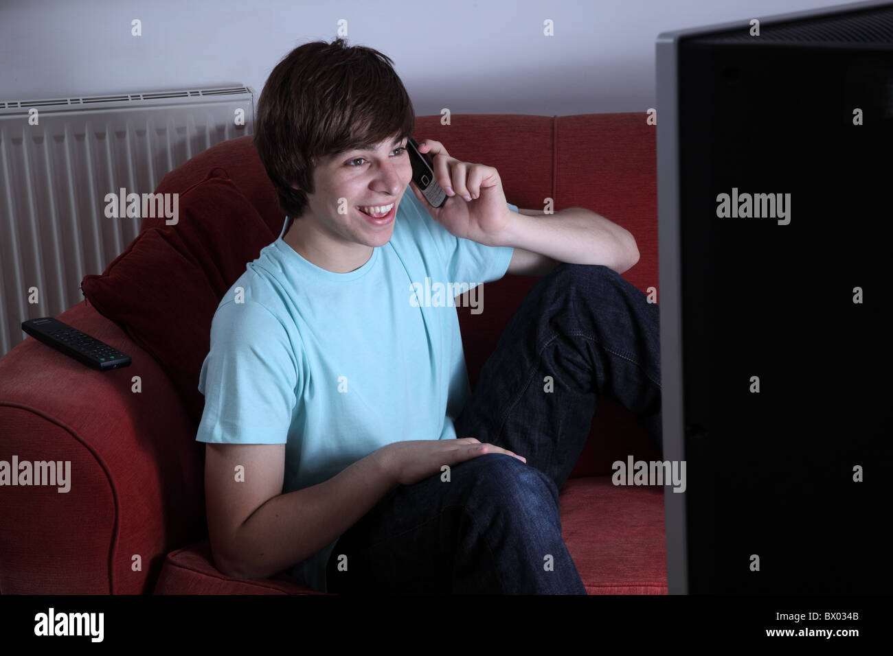 Young male holding a phone smiling and watching tv Stock Photo