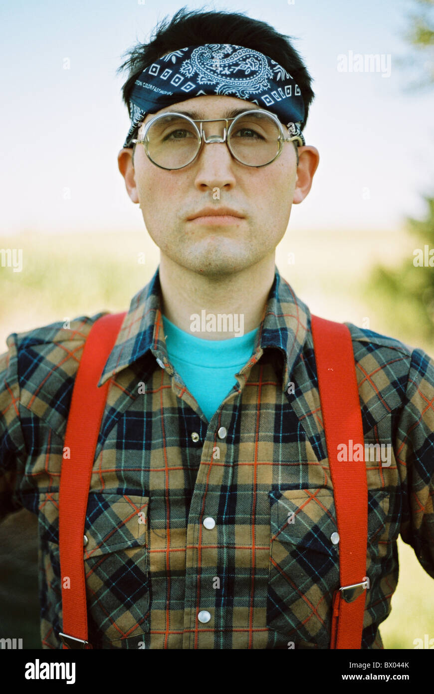 A man wearing bomber glasses, a bandana, flannel, and suspenders. Stock Photo