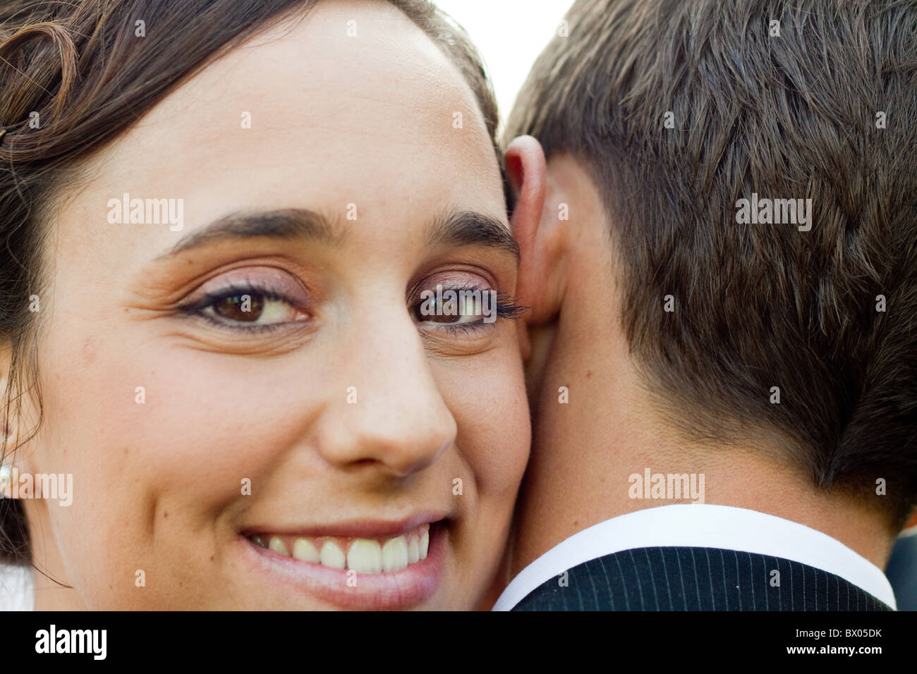 A wfe looks over her husband's shoulder as she embraces him. Stock Photo