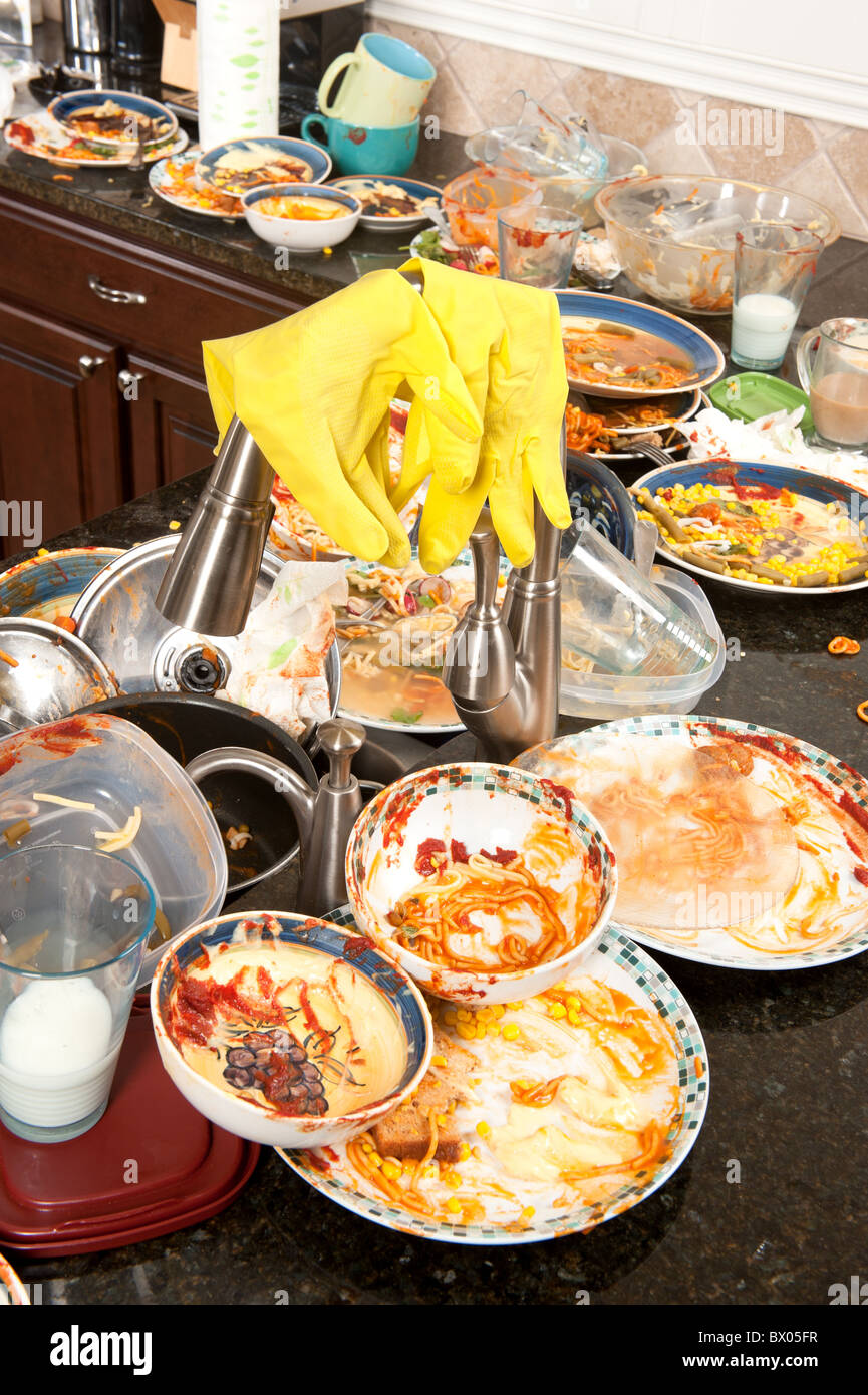 A pair of yellow dish washing gloves hangs on a sink faucet surrounded by filtyh dishes. Stock Photo