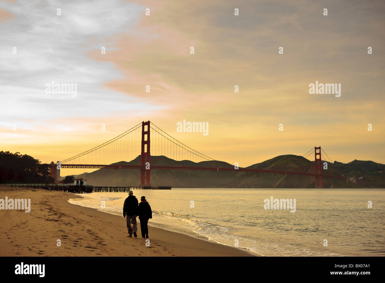 Couple walking at sunset towards Golden Gate Bridge Stock Photo