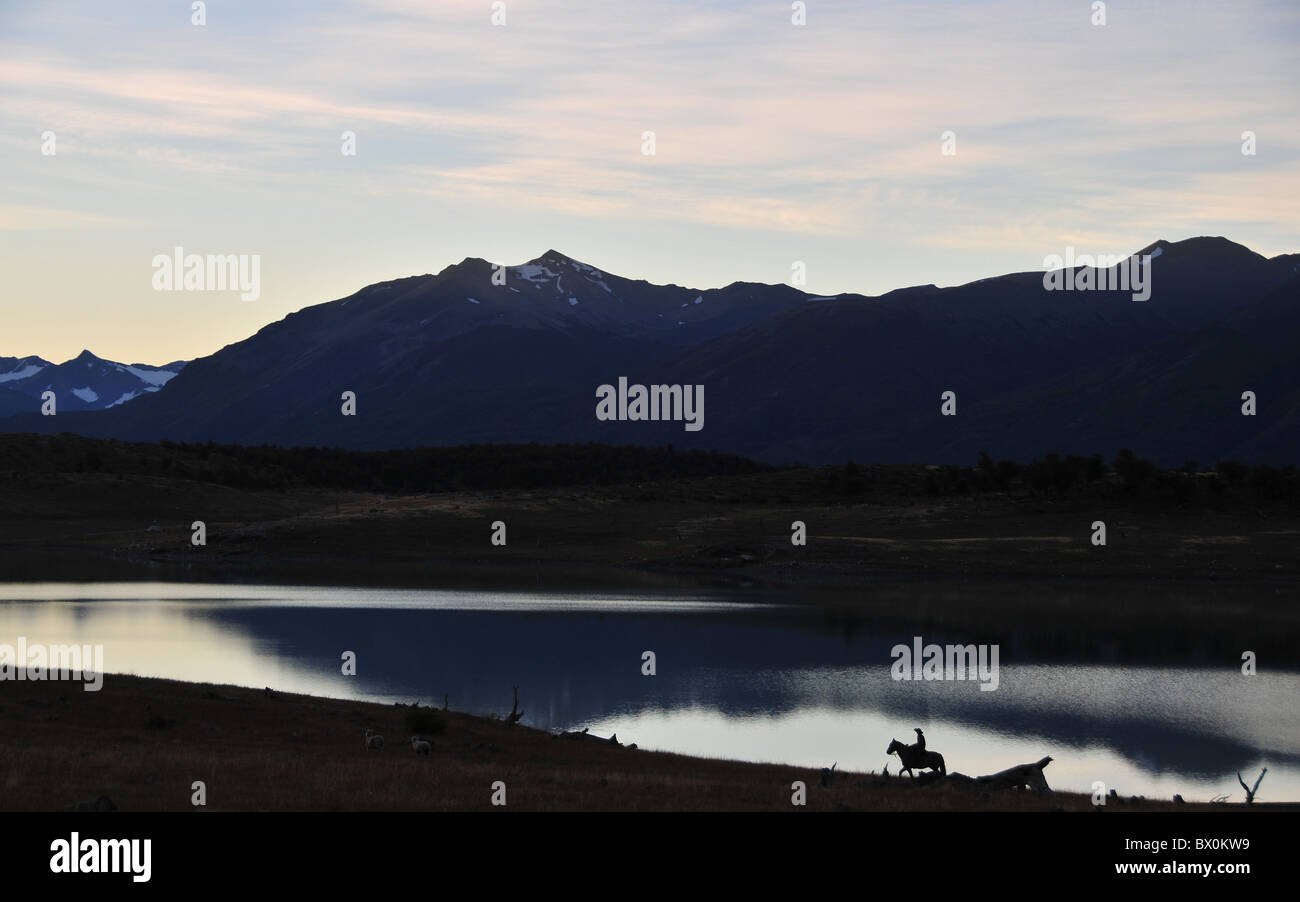 Sunset silhouette of Andean peaks and horse-back gaucho reflecting in the still waters of Lago Roca, Andes, Patagonia, Argentina Stock Photo