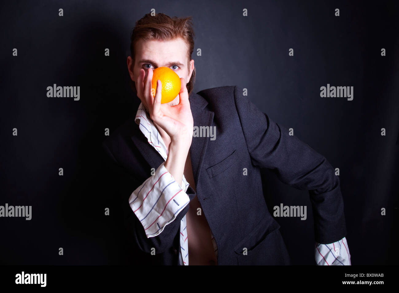 young man with an orange in his hand on black background Stock Photo