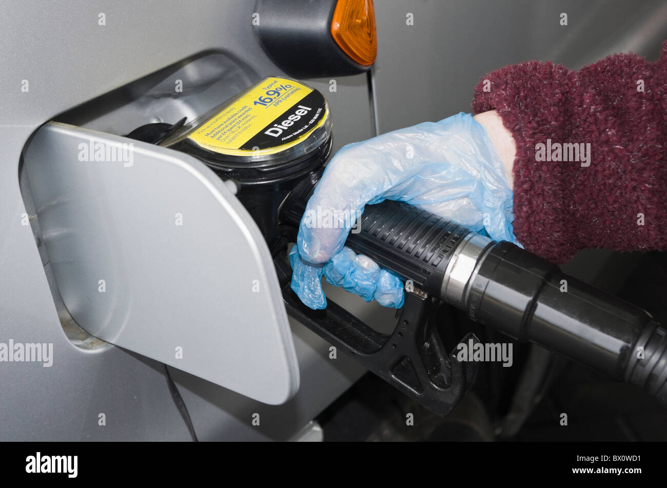Motorist wearing plastic disposable gloves whilst holding a fuel pump to fill a vehicle with Diesel at a gas filling station. UK Britain Stock Photo