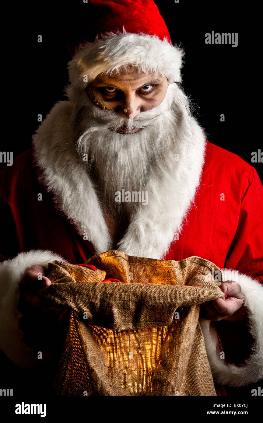 a scary looking santa holding a glowing present bag Stock Photo