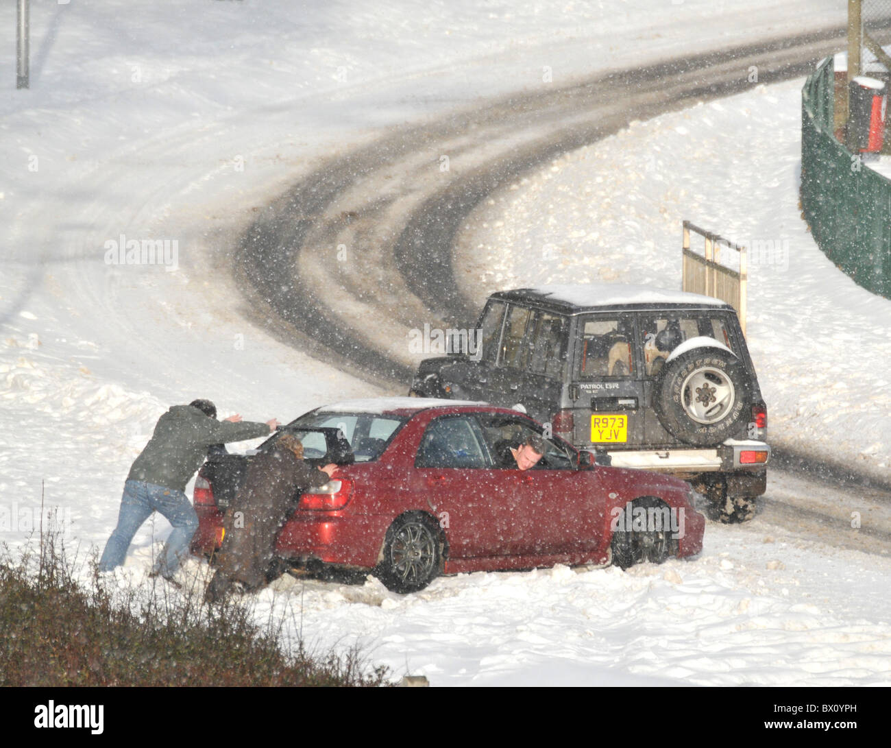 A couple try pushing a trapped car out of a snowdrift. Stock Photo