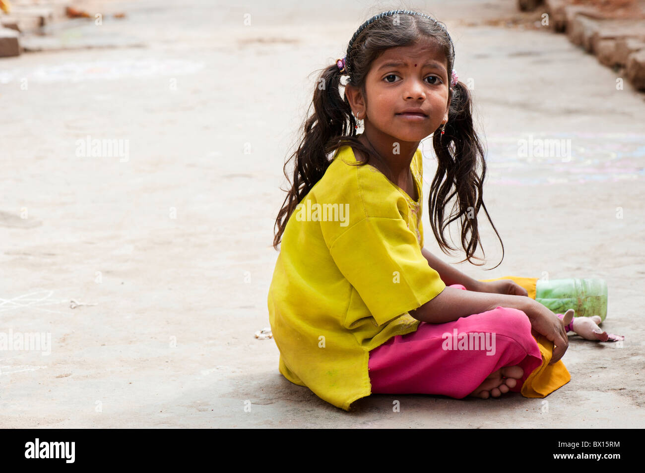 Smiling happy Indian village girl with a soft toy sitting in the street. Kothacheruvu, Andhra Pradesh, India Stock Photo