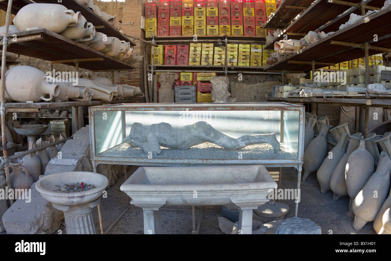 Store room at Pompeii with shelves of amphorae and the cast of a citizen, buried alive by volcanic ash, in a glass case Stock Photo