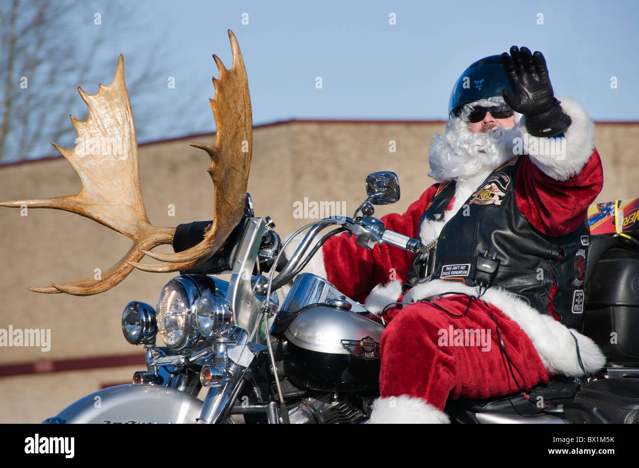 A man in a Santa costume rides his motorcycle with reindeer antlers on