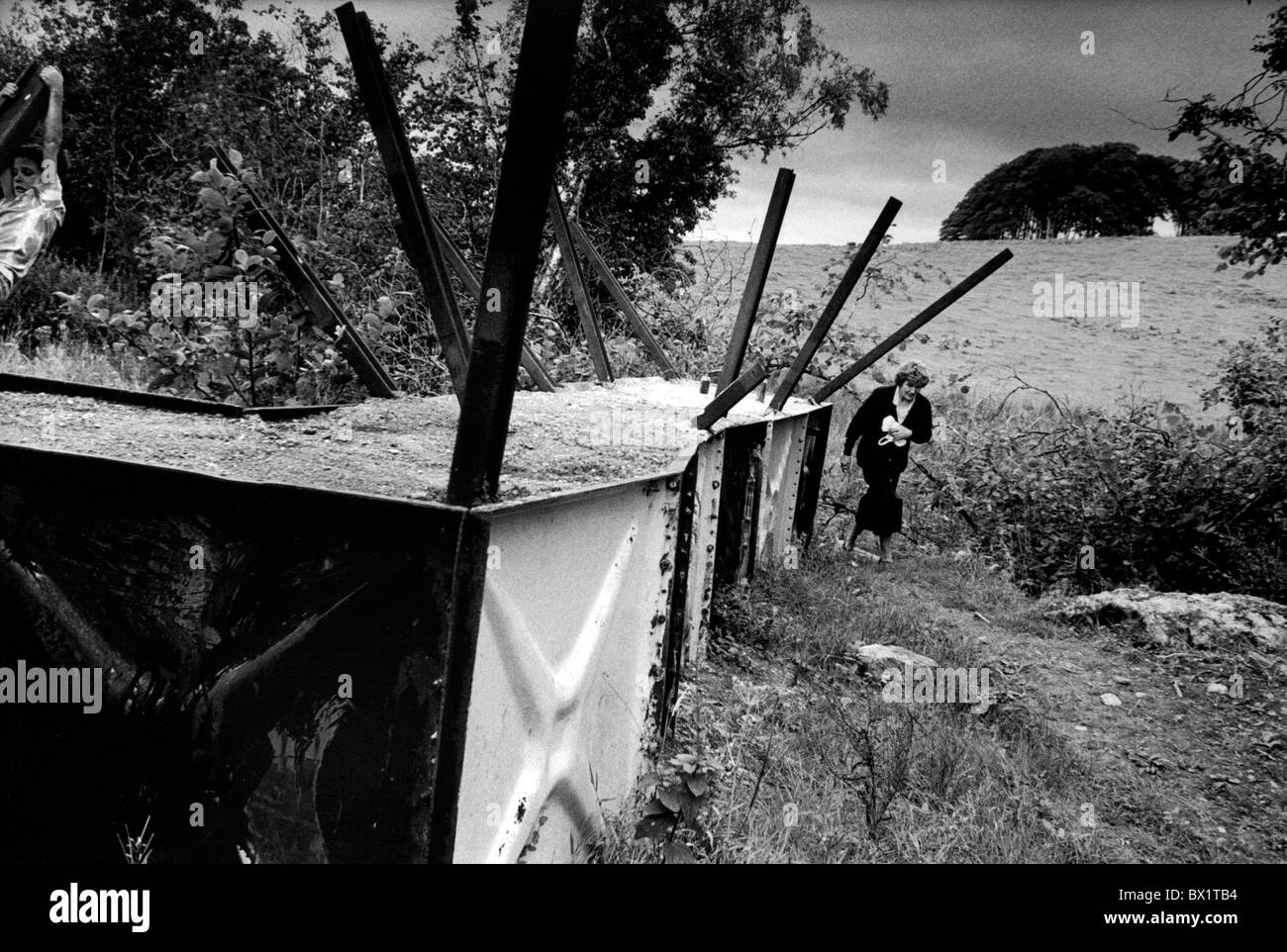Border road blocked by barricade at the border between the Republic and the North of Ireland. Woman makes the crossing. Stock Photo